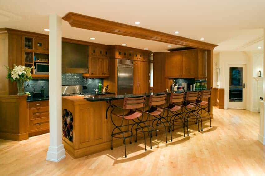 棕色厨房有白色的柱子和木制橱柜，与半岛相匹配，配有内置的酒架。它在浅色硬木地板上铺设了金属柜台椅。