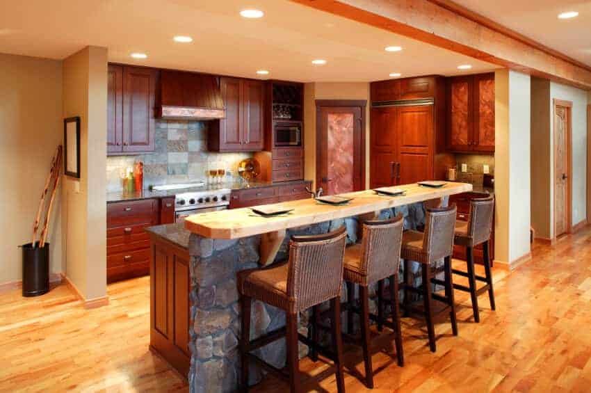 这间厨房设有红木橱柜和一个石头两层岛，配有柳条柜台椅。它由安装在常规米色天花板上的凹进式灯照明。
