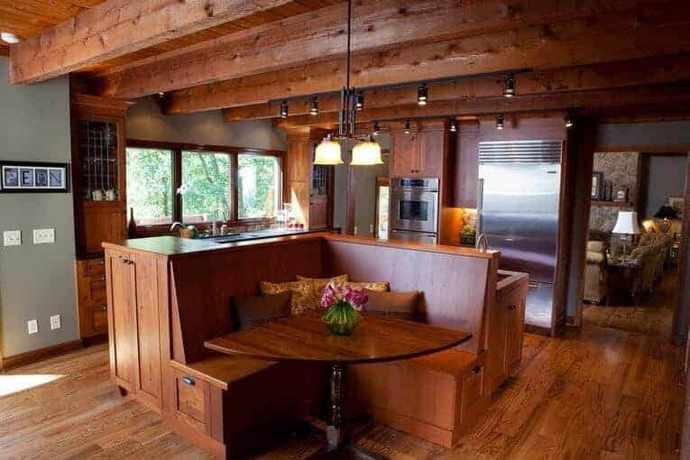 餐厅厨房，硬木地板和木梁天花板安装轨道灯和玻璃挂件。它包括木制橱柜和配套的岛台，岛上有一个早餐角。