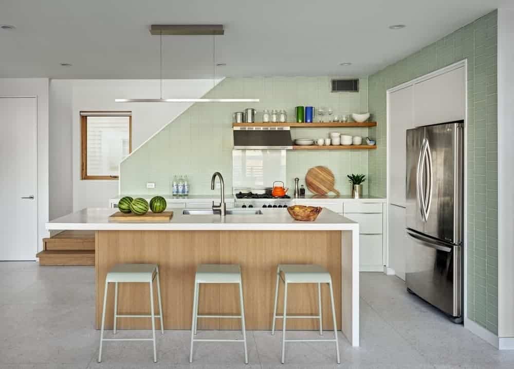 小屋厨房有混凝土地板和绿色瓷砖墙，配有嵌入式橱柜和电器。餐厅中间有一个早餐吧台，旁边摆着光滑的凳子。