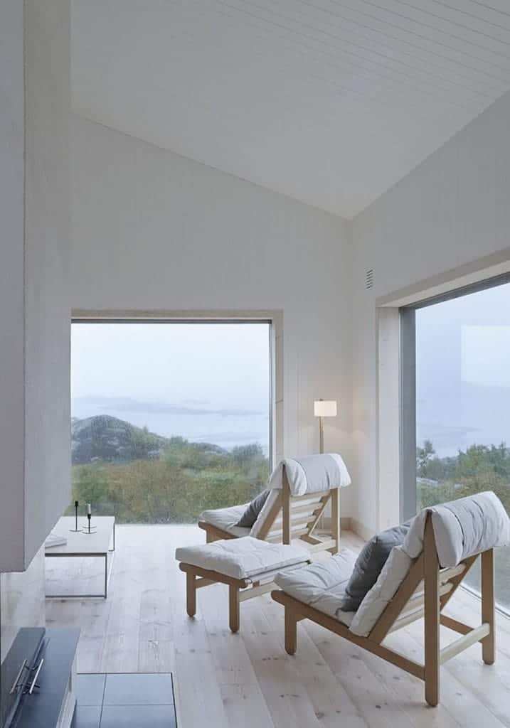 这间小屋风格的客厅四周环绕着巨大的玻璃墙，可以看到周围山腰的美景。这是一对木质软垫椅子的重点，它们与浅色硬木地板搭配得很好。