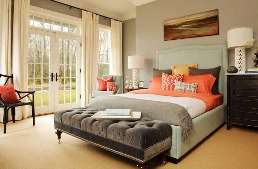 这个乡村风格的主卧室的亮橙色色调与浅绿色的床架和软垫床头板、浅灰色的墙壁、米黄色的地毯地板和白色的天花板形成鲜明的对比。从玻璃门射进来的自然光使这些房间更加明亮。