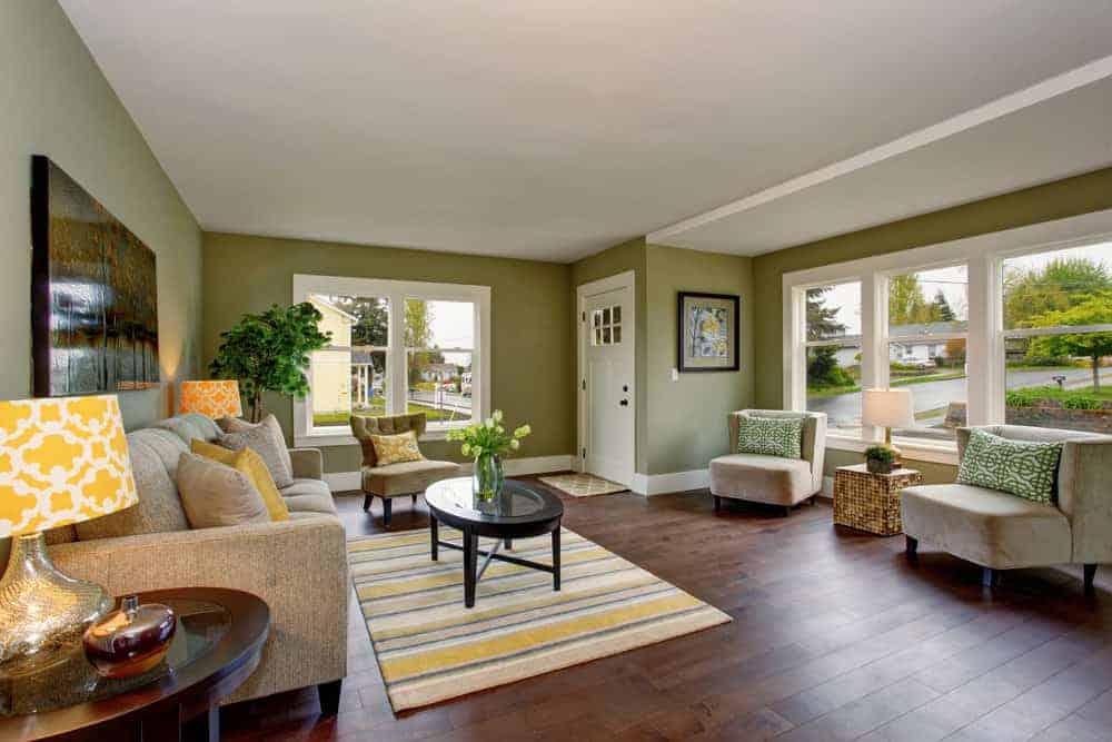 宽敞的乡村风格客厅，橄榄绿的墙壁和硬木地板，配有舒适的沙发套装和一张小桌子，上面放着一块小地毯。