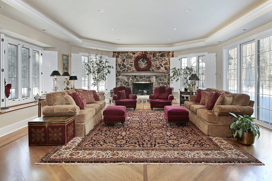 宽敞的正式客厅，配有一对优雅的沙发和带脚凳的红色天鹅绒座椅，放置在覆盖硬木地板的大面积地毯上。那里有一座巨大的石头壁炉和一个托盘天花板。