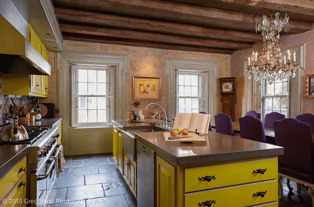 一间内吃式厨房提供黄色橱柜和配套的岛式吧台，吧台上装有华丽的锻铁五金和一个船水槽。它有砖地板和木梁天花板安装了一个花式蜡烛吊灯。