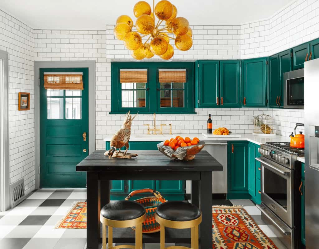 一盏当代风格的枝形吊灯悬挂在黑色的厨房岛台上方，配以软垫吧台凳。这间厨房拥有不锈钢电器以及翡翠绿的橱柜和门，在白色地铁后挡板瓷砖的映衬下显得格外显眼。