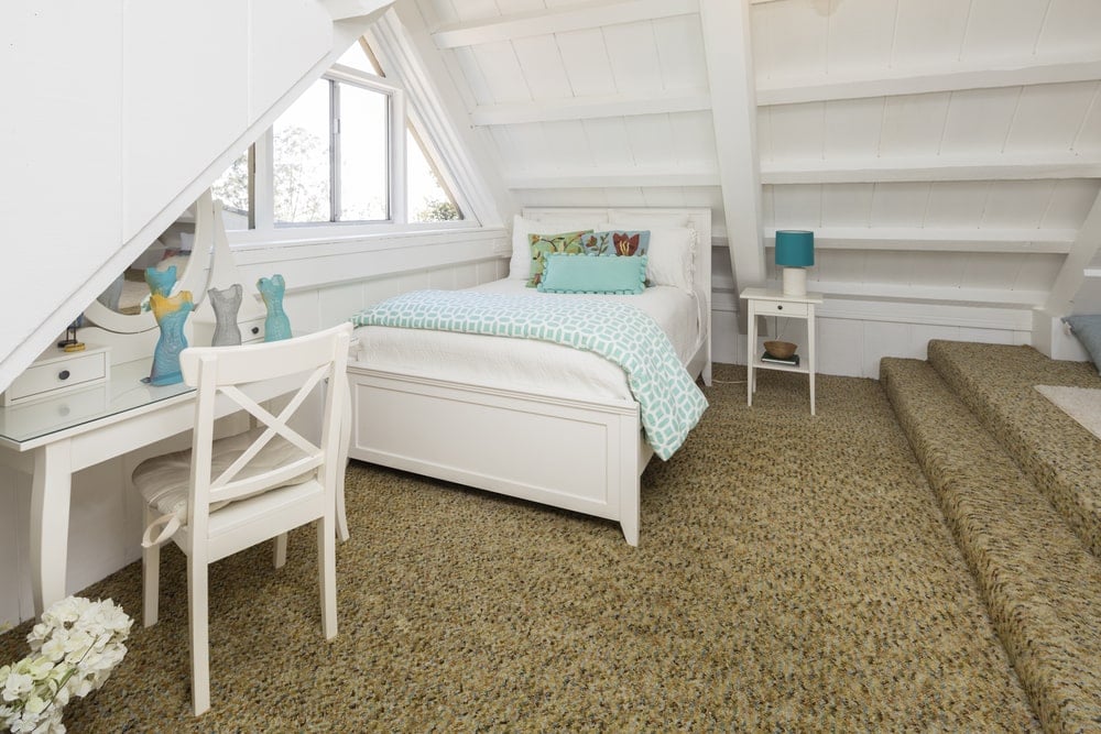 这是一个漂亮的孩子的卧室，位于房子的阁楼。它提供了一种独特的美学，它有一个低矮的白色大教堂木制天花板，在白色的床和桌子旁边有一个三角形的窗户。在棕色地毯的衬托下，这个很显眼。