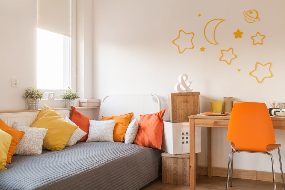 这个孩子的卧室有有趣的橙色细节，为木桌和硬木地板的中性元素赋予了生命和古怪的一面。这也为朴素的白色墙壁和小屋床的灰色床单增添了一抹色彩。