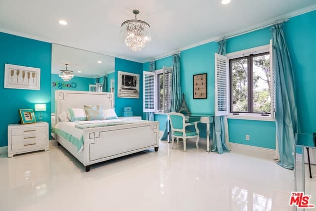 明亮的蓝色墙壁给这个地中海风格的卧室一个独特的个性。白色的地板和白色的天花板加强了这一点，与白色的雪橇床相匹配，两侧是白色的床头抽屉，床头板后面的大镜子补充了这一点。