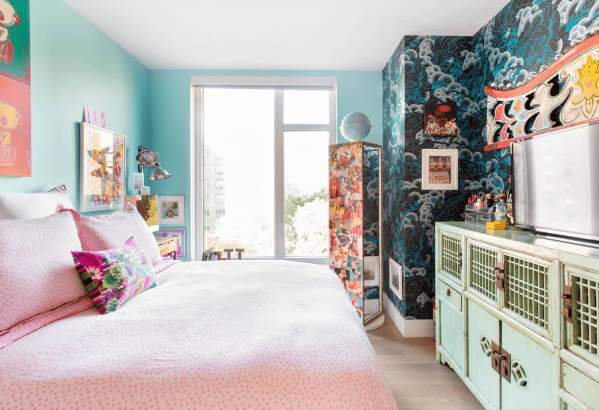 这间卧室展示了一个旋转的全长镜子和粉红色的圆点床，面对着破旧的绿色橱柜。它包括安装在水色墙壁上的彩色艺术品。