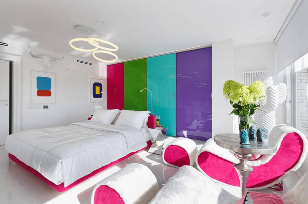 时尚的卧室拥有粉红色的白色家具，以及内置的衣柜，配有多色门。它由悬挂在月台床上的圆形吊灯照亮。