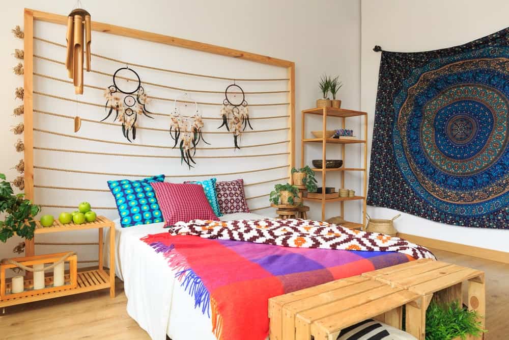 波西米亚风格的主卧室设计华丽的挂毯和可爱的捕梦网，挂在白色的床上，强调了多种颜色的枕头和毛毯。
