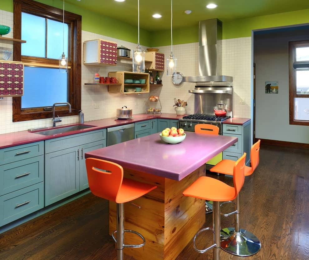 色彩缤纷的厨房拥有蓝色的橱柜和紫色的顶部岛，搭配充满活力的橙色凳子。它有天然硬木地板和绿色天花板，天花板上装有嵌入式灯。