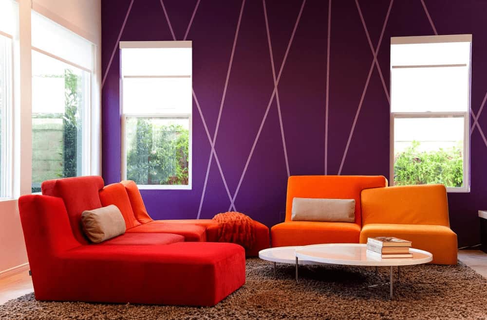 现代客厅以圆形模块化咖啡桌和充满活力的橙色座椅为特色，与紫色墙壁形成鲜明对比。它有棕色的蓬松地毯和玻璃窗户，可以让自然光进来。