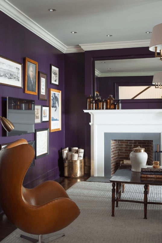 一把现代风格的琥珀色椅子正对着木咖啡桌，对面是砖砌的壁炉，壁炉的边框是灰色的，壁炉架是白色的。这间房间有一面相册墙，深色硬木地板，上面铺着灰色的小地毯。