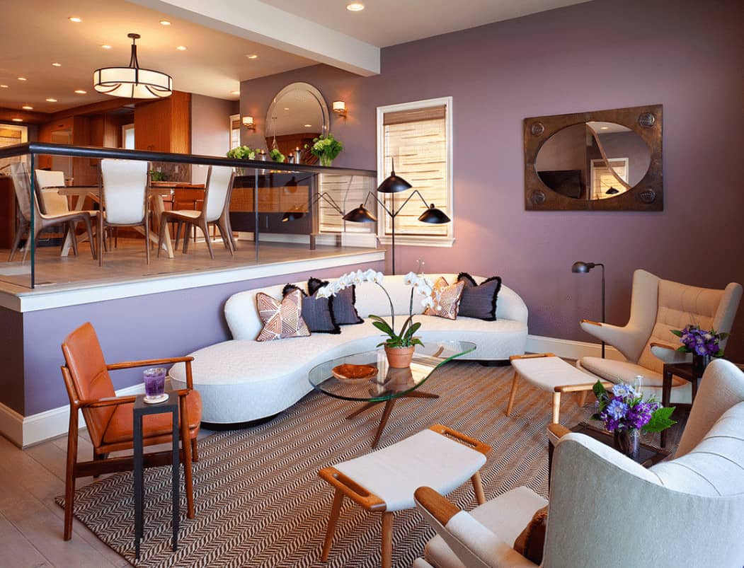 开放式的起居区，有光滑的沙发和现代扶手椅，周围是玻璃面咖啡桌，桌子放在引人注目的地毯上。它有宽阔的木板地板和淡紫色的墙壁，并配有一面镜框镜子。