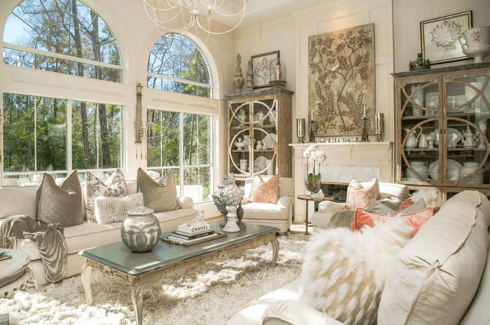 壁炉旁边有一对木制展示柜，壁炉上装饰着一幅树叶艺术品。它的白色座椅环绕着优雅的咖啡桌，大拱形窗户俯瞰着迷人的森林。