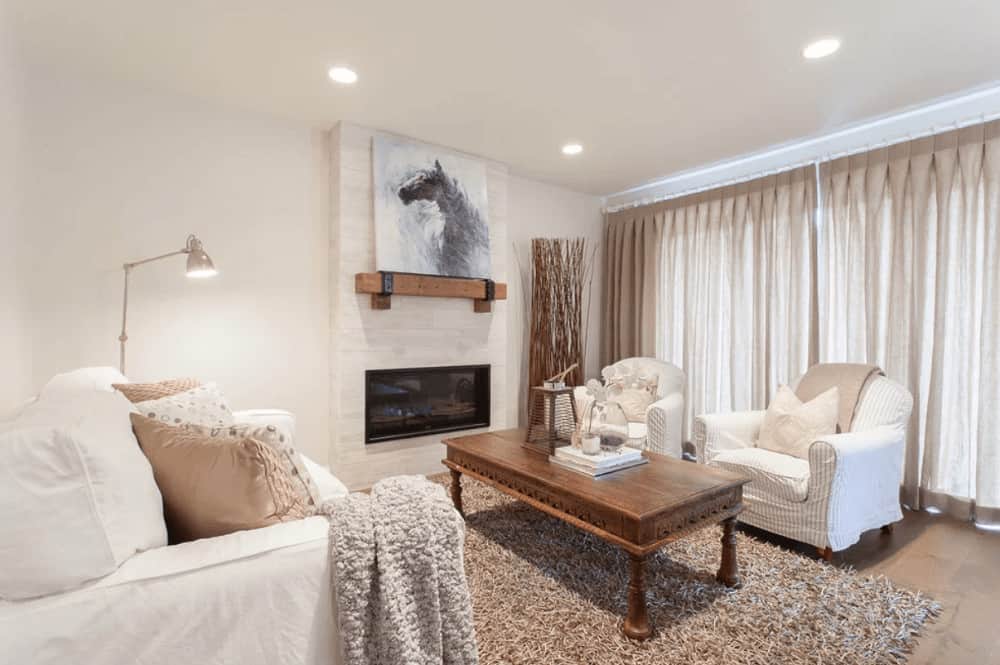 白色的客厅里有舒适的座椅和一张木制咖啡桌，上面铺着蓬松的地毯。它包括一个衬有木制壁炉架的壁炉，上面有可爱的马艺术品。