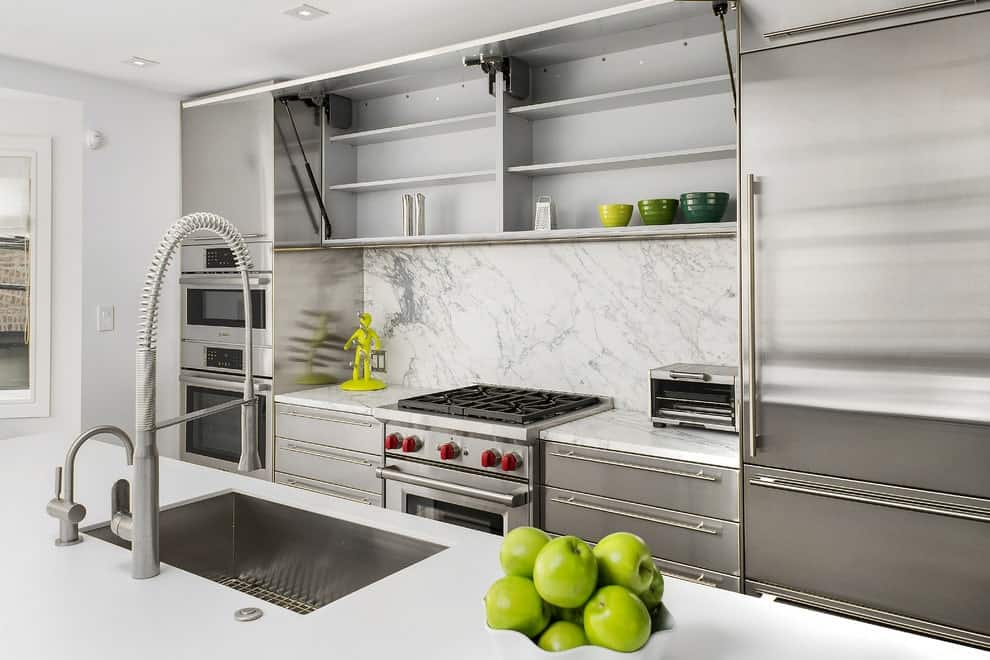 极简主义厨房与白色大理石后挡板和嵌入器具隐藏在不锈钢橱柜。它包括一个石英顶部岛酒吧，配有水槽和铬固定装置。