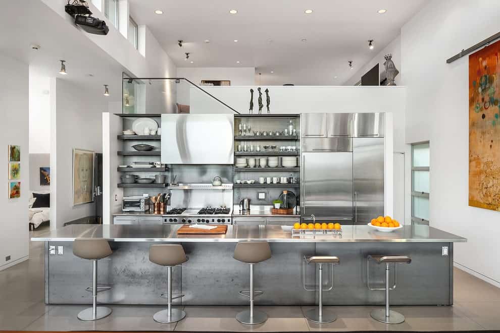 开放式概念厨房提供不锈钢电器和橱柜，以及安装在金属后挡板上的浮动货架。它包括一个岛上的酒吧，里面排列着灰色的凳子。