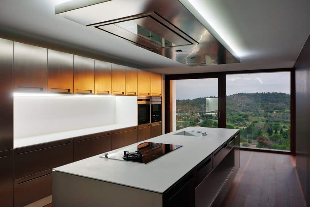 光滑的厨房，宽木板地板和全高玻璃俯瞰一个令人惊叹的景色。它包括黑色电器和不锈钢橱柜，与配有水槽和内置灶台的厨房岛相辅相成。
