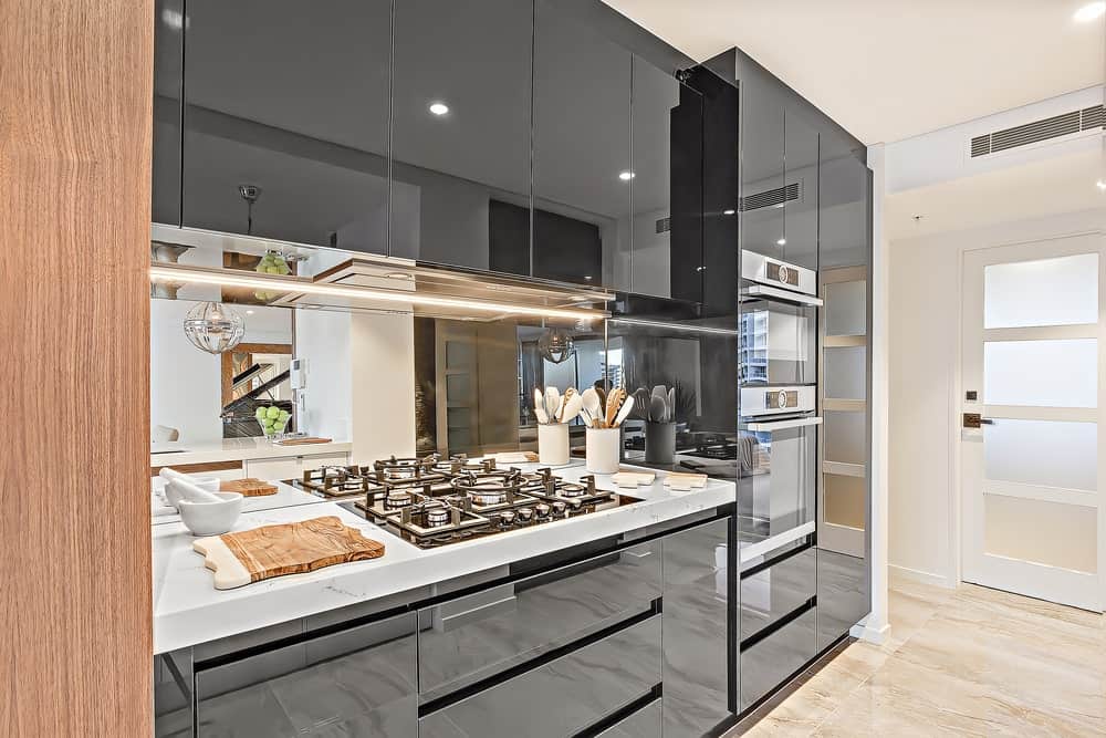 白色磨砂玻璃门通往这间豪华厨房，配有镜面后挡板和高玻璃橱柜，与白色大理石台面形成鲜明对比，厨房配有内置灶台。