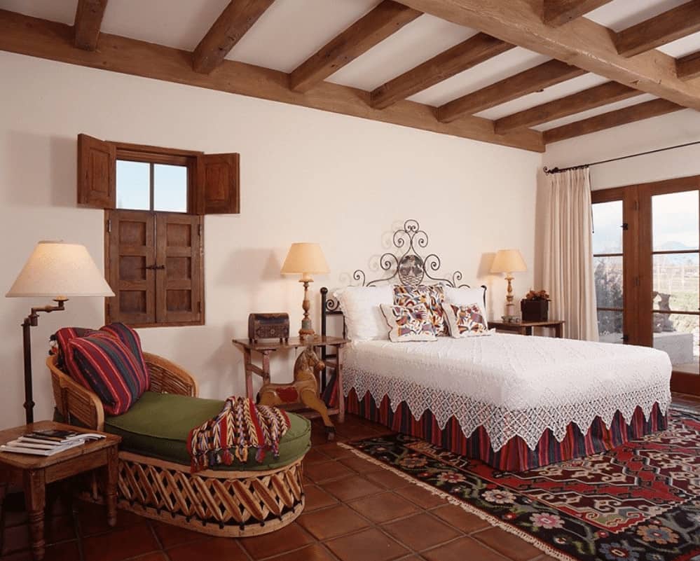 华丽华丽的床放在花地毯和陶土地板上，在西南卧室展示木制床头柜和一个时尚的躺椅，上面有绿色靠垫。