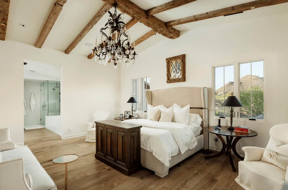 白色的主卧室有宽阔的木板地板和玻璃窗，可以看到壮观的山景。它有舒适的座椅和米色的翼背床，由一盏漂亮的枝形吊灯照亮。