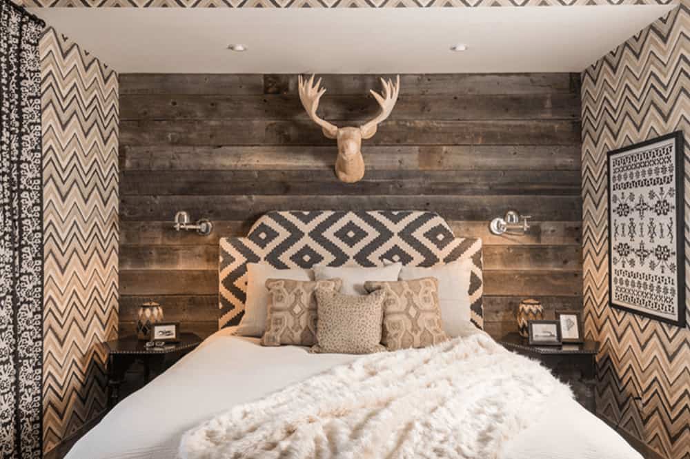 覆盖在雪佛龙壁纸和乡村木板，这个主卧室拥有鹿头装饰和舒适的床两侧的六边形床头柜和铬烛台。