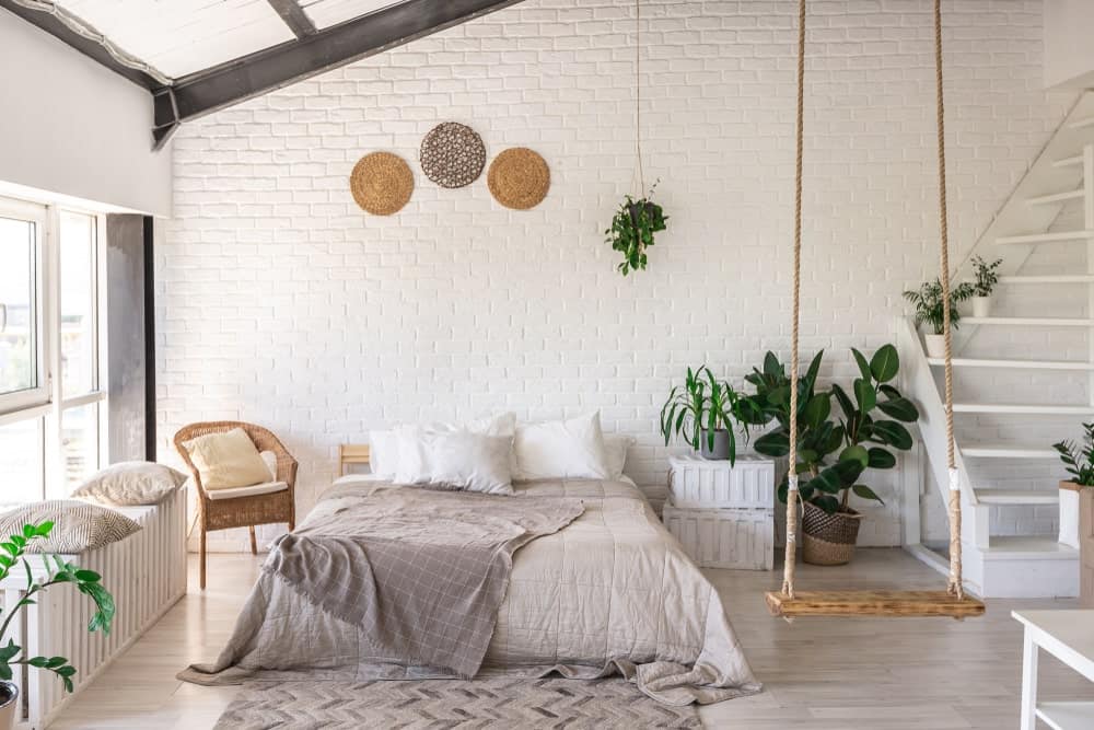 白墙砖口音增加纹理在这个热带的卧室里有秋千和舒适的床上,坐在灰色的雪佛龙地毯在光硬木地板。