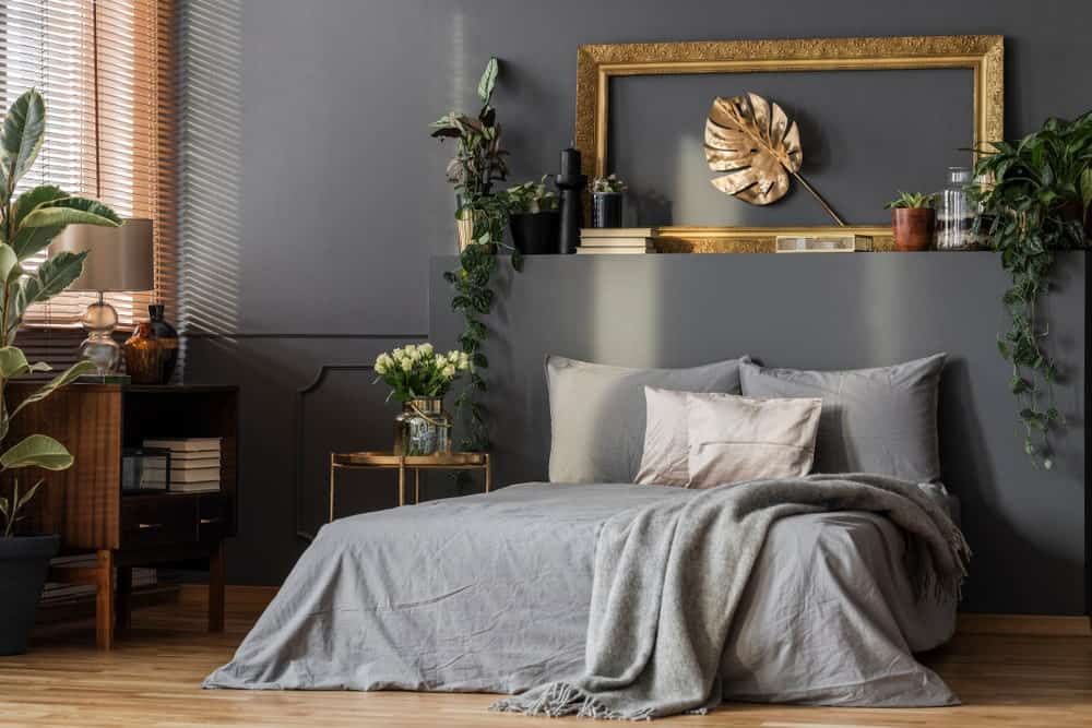 这个主卧室装饰着盆栽和一个可爱的叶墙艺术框架在华丽的黄金。它安装在平台床,穿着灰色的床上用品。