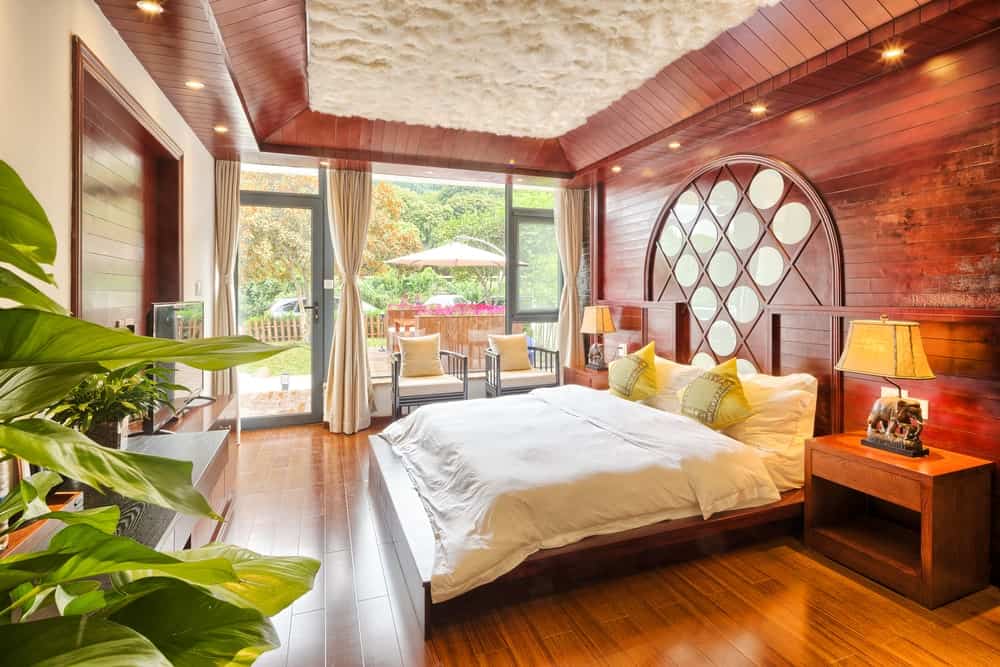 温暖的卧室与丰富的硬木地板和变形盘天花板凹式灯包围。它包括灰色圆背椅子和一个舒适的床上木质床头柜之间加上大象台灯。