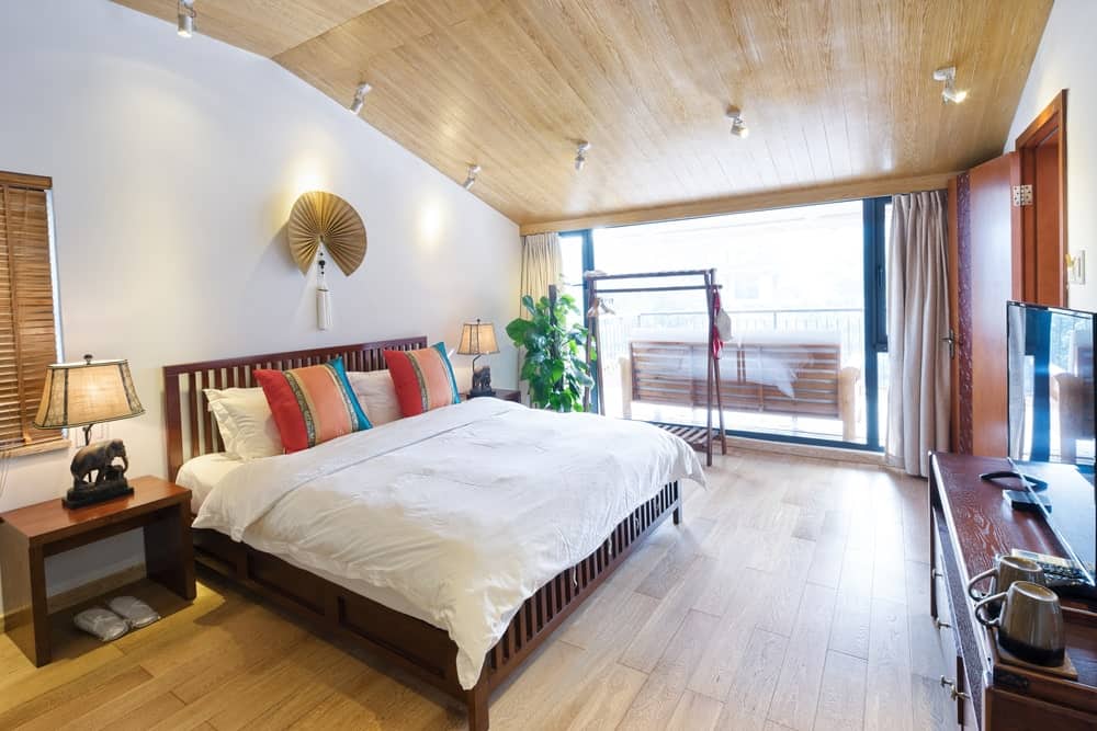 舒适的主卧室和一个木制的床和床头柜上加上大象台灯。它被白色轨道灯安装在拱形的天花板穿着光木板条。