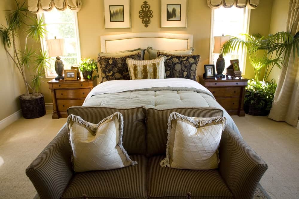 这主卧室有一个白色的皮革沙发床和条纹加上流苏的枕头。木质床头柜,穿着可爱的米色valances框架窗口。