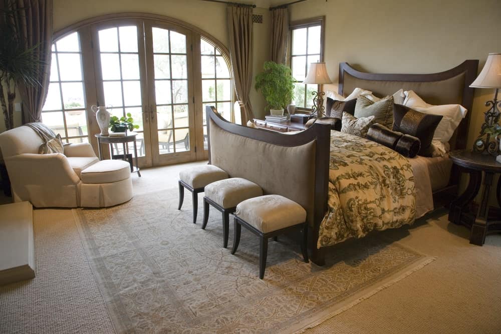 热带主卧室有一个白色的躺椅和缓冲软垫床在其结束凳子,坐在老式面积地毯。