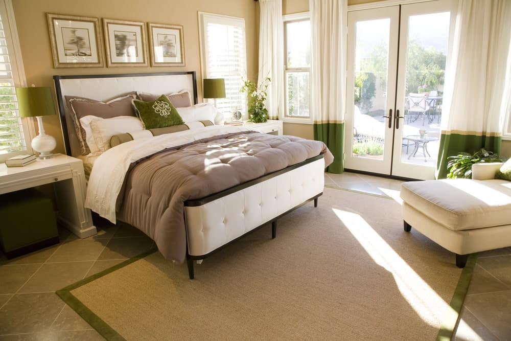 米色的主卧室窗帘的微妙的绿色口音,抱枕和灯罩,坐在白色的床头柜上。它有一个白色的躺椅和簇绒床与黄麻地毯和石灰岩地板。