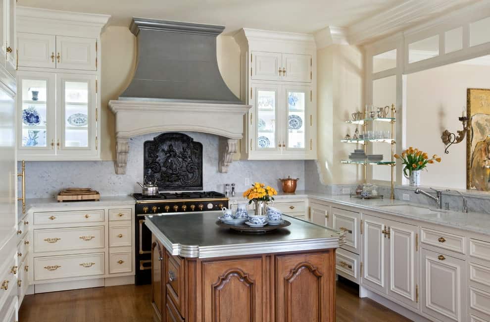 这间厨房拥有对比鲜明的黑色范围和白色橱柜，强调黄铜五金。它包括一个木制的中央岛台，灰色的台面与通风罩互补。