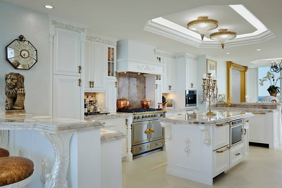 豪华厨房提供白色橱柜和配套的岛，顶部有大理石柜台和黄铜烛台。它由安装在托盘天花板上的华丽的半平光灯照亮。