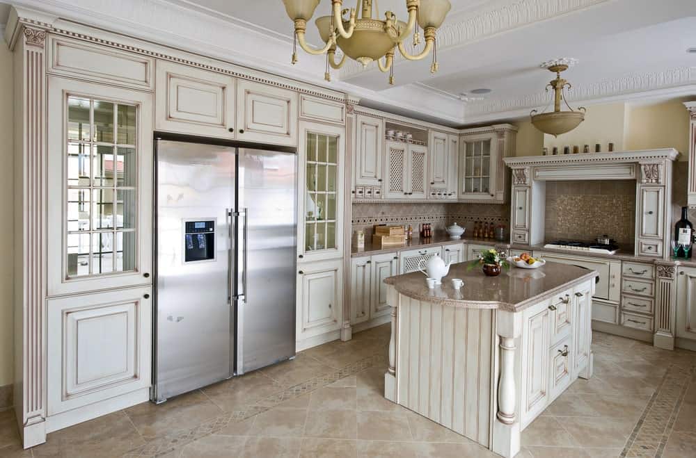 这间厨房里有一个不锈钢冰箱，两侧是玻璃前柜，还有一个床头板岛台，上面有一个花岗岩柜台。它包括vintage <a class=