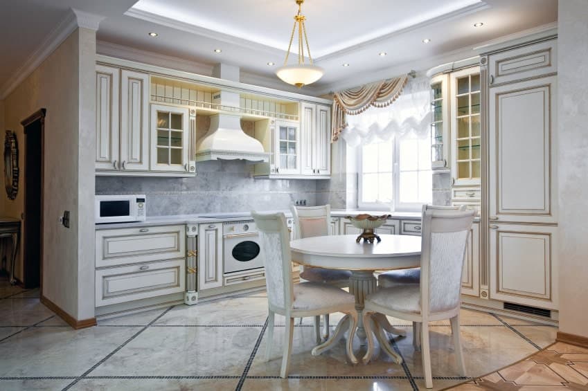 维多利亚式厨房，大理石地板，托盘天花板上安装有嵌入式灯和玻璃圆顶吊坠。它包括白色橱柜和圆形餐具，上面有一个装饰碗。