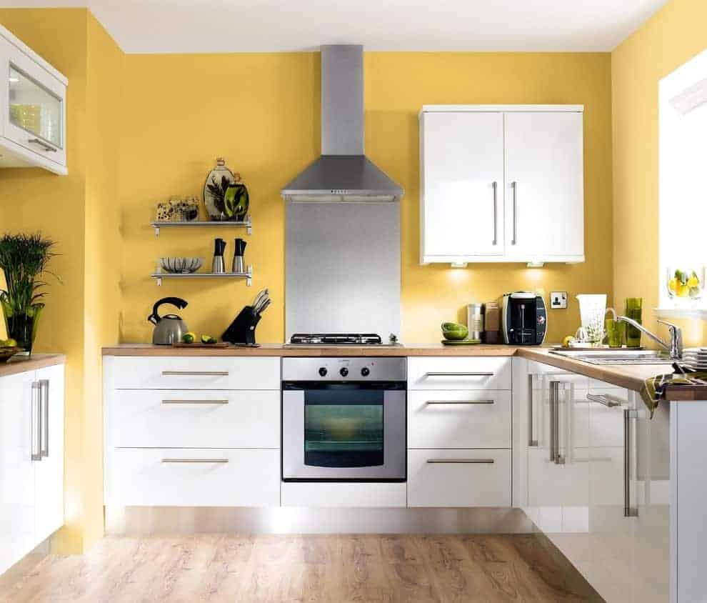 光滑的厨房拥有白色的橱柜和固定在黄色墙壁上的浮动货架。它有天然硬木地板和玻璃窗，让自然光线进来。