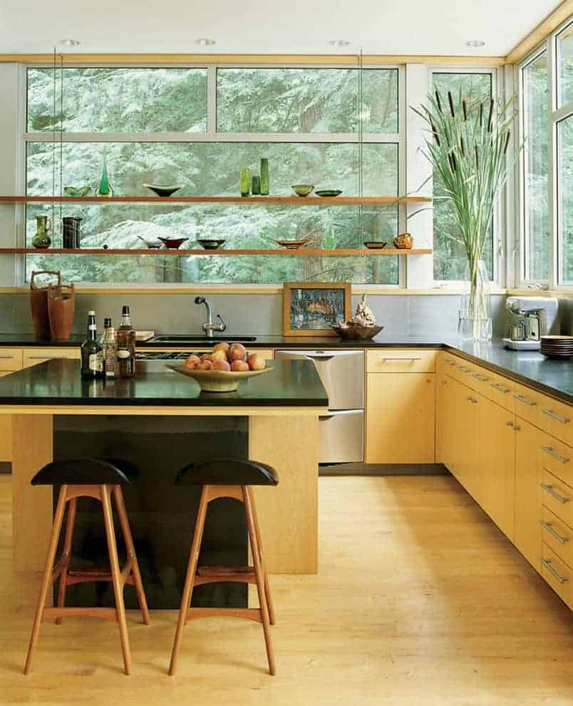 新鲜的厨房设有轻木橱柜和配套的早餐岛，与硬木地板融为一体。它有黑色的台面和漂浮的架子，靠着玻璃镶板的窗户，俯瞰着迷人的森林。