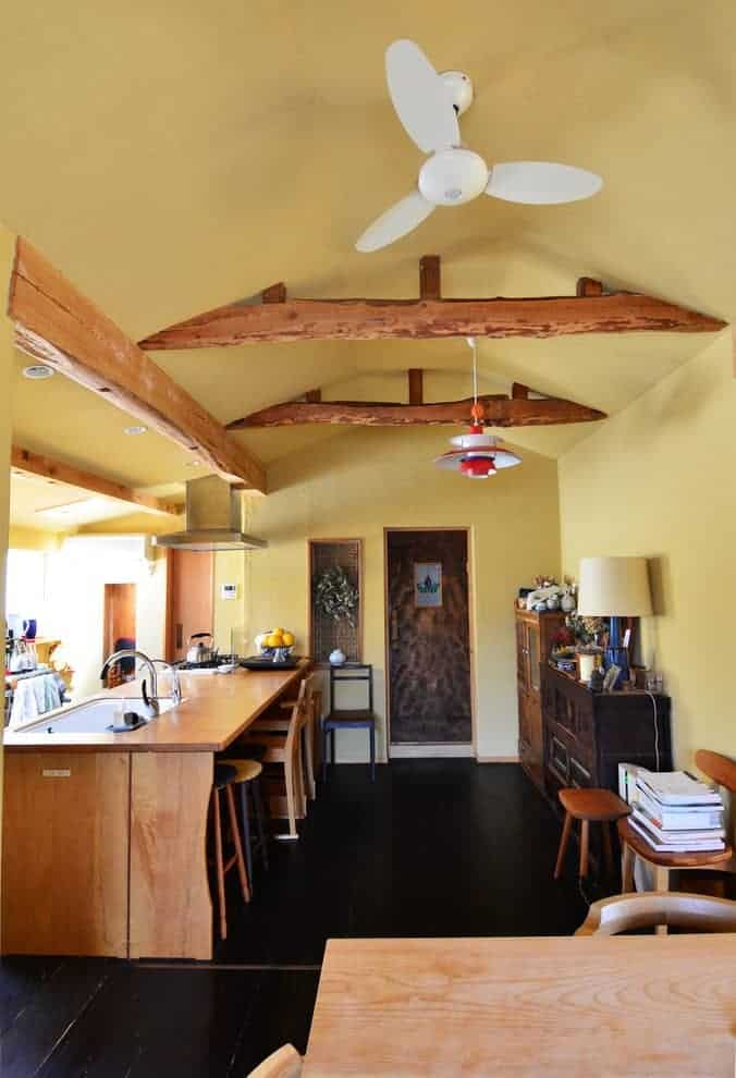 亚洲厨房，黑色瓷砖地板和黄色拱形天花板，内衬乡村梁。它包括木制橱柜和早餐吧，配有瓷水槽和铬固定装置。