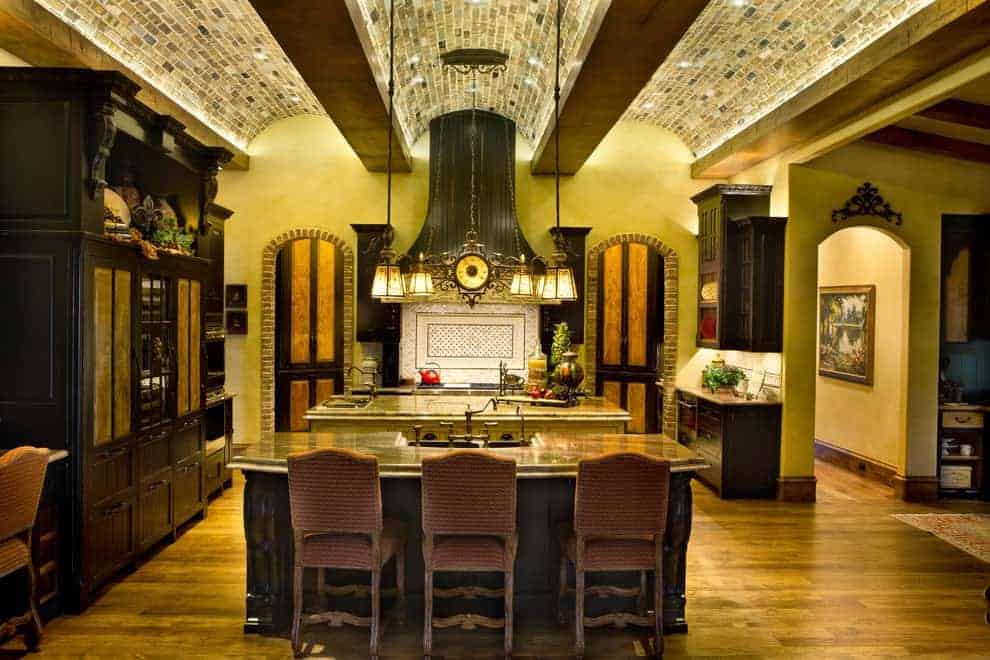 复古吊灯的环境光在这个厨房里创造了温暖舒适的感觉，双岛酒吧和暗木橱柜衬着黄色的墙壁。它有硬木地板和令人惊叹的桶形穹顶天花板，天花板由砖块覆盖。