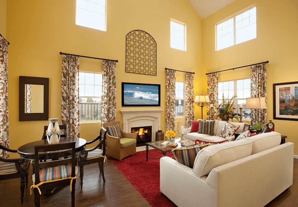 高天花板的客厅，硬木地板和装饰着花卉窗帘的玻璃窗。房间里有一座壁炉和几张白色沙发，还有一张放在红色地毯上的玻璃咖啡桌。