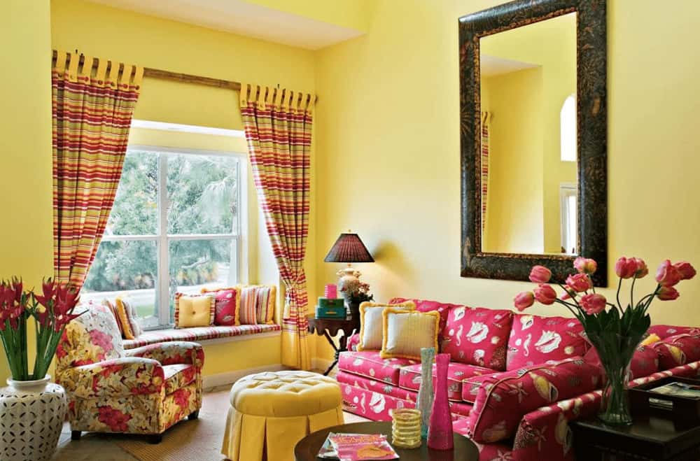 一面大镜子悬挂在红色部分的上方，旁边是一张花扶手椅和一个簇绒的圆形奥斯曼。侧面有一个靠窗的座位角落，配有小枕头和条纹靠垫，与窗帘相匹配。