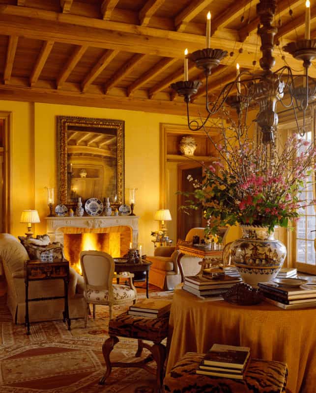 温暖的客厅，有壁炉和舒适的座位，上面铺着印花地毯。它包括一张桌子，周围有软垫凳子，由从木梁天花板上悬挂的蜡烛吊灯照亮。