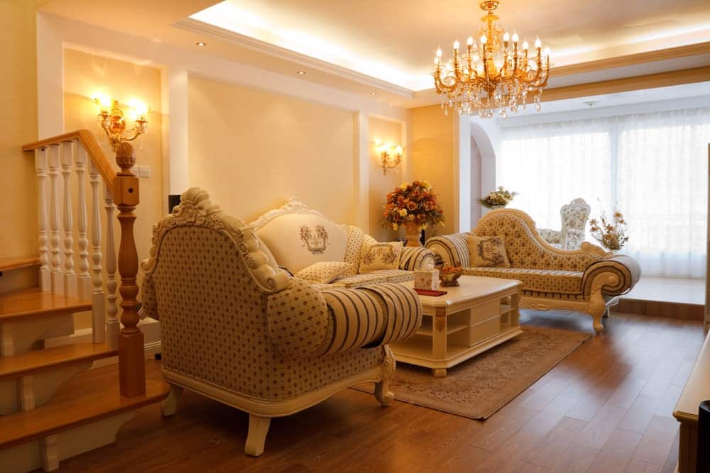 配套的黄铜壁灯和花哨的枝形吊灯照亮了这个起居区，提供了优雅的座椅和一张咖啡桌，咖啡桌的架子放在宽阔的木板地板上的经典区域地毯上。