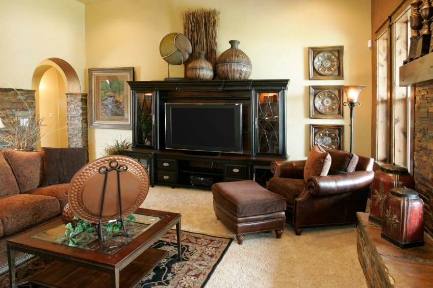 这间客厅的特色是棕色皮革躺椅和组合沙发，搭配木制咖啡桌。房间里装饰着古色古香的壁饰和花瓶，花瓶放在一个深色的木柜上。