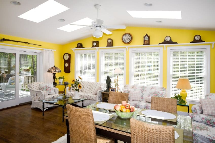 起居区域的黄色墙壁上布满了各种时钟和白色框架的窗户，地板是硬木地板，拱形天花板上安装了天窗和风扇。